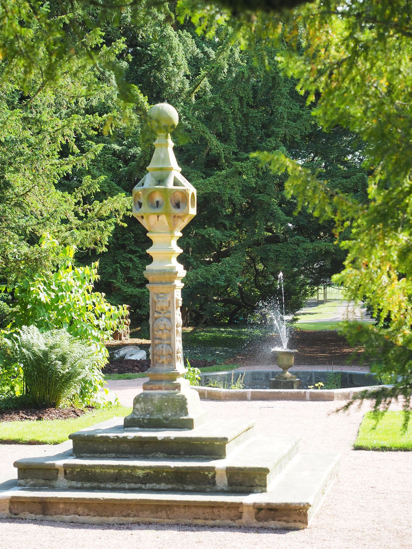 A carved stone sundial on a tall column beside a fountain